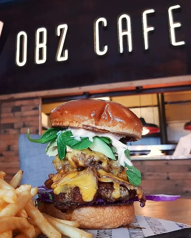 A stacked burger and fries in front of the Obz Café sign