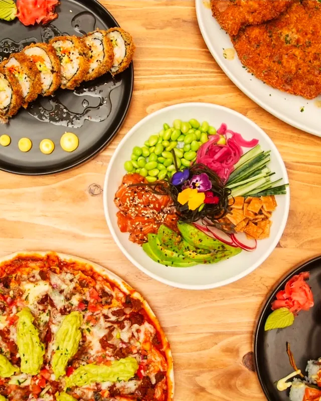 Sushi, a poke bowl and pizza on a wooden table